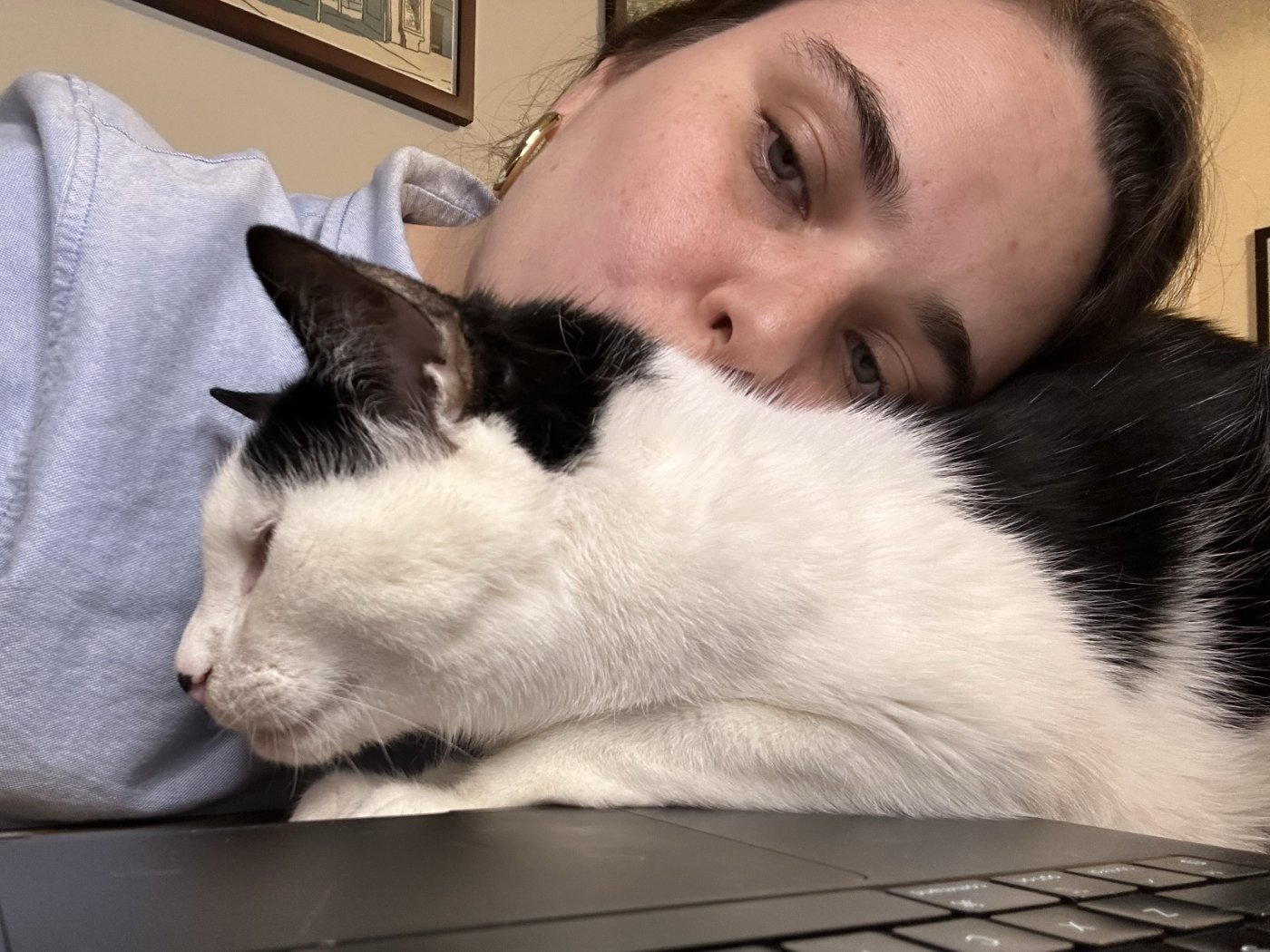 Andrea resting her head on her black and white cat, who is asleep across her laptop